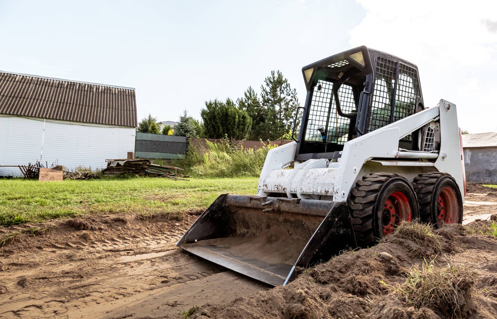 Skid steer with a bucket preparing cleared ground beside a building