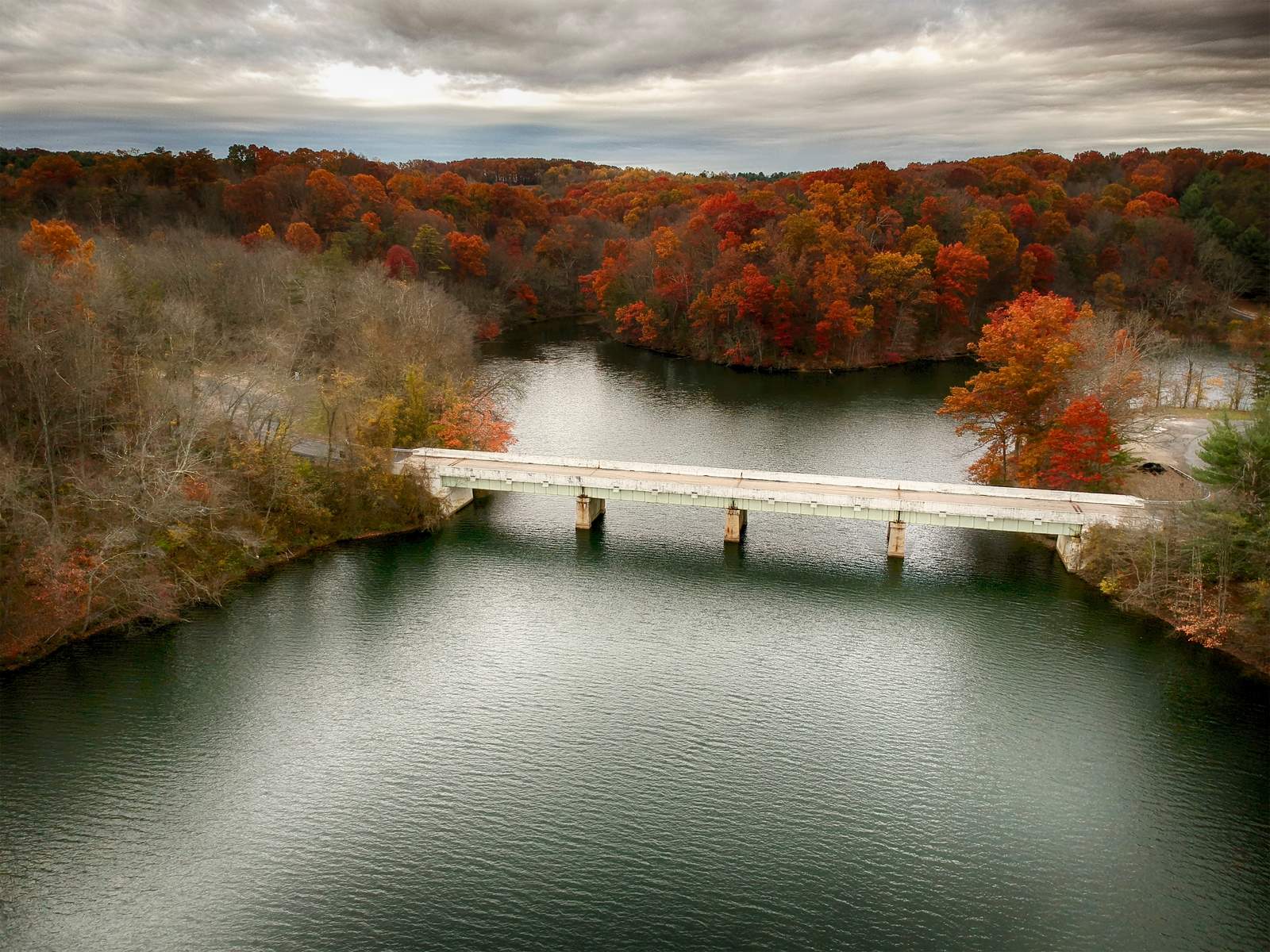 Aerial view of a bridge crossing a reservoir surrounded by red and orange fall trees